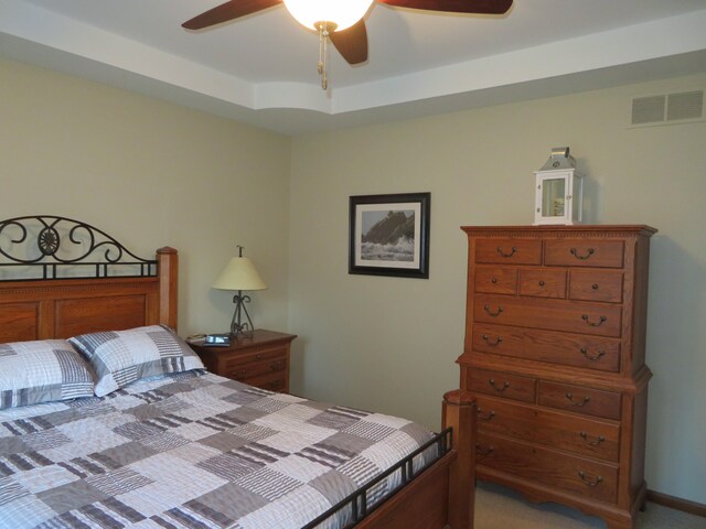 bedroom featuring a raised ceiling, ceiling fan, and light carpet