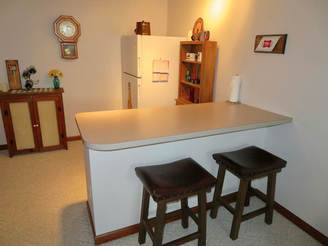 kitchen featuring a kitchen bar, kitchen peninsula, light carpet, and white refrigerator