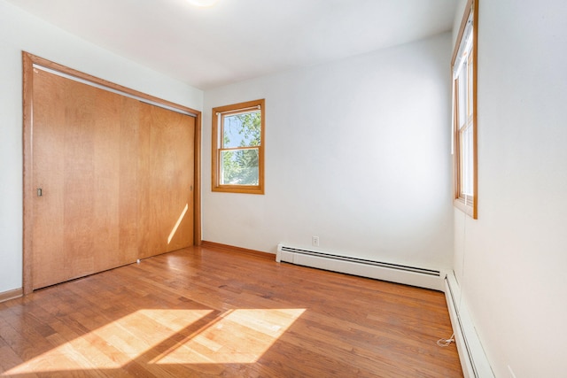 unfurnished bedroom with hardwood / wood-style floors, a closet, and a baseboard heating unit