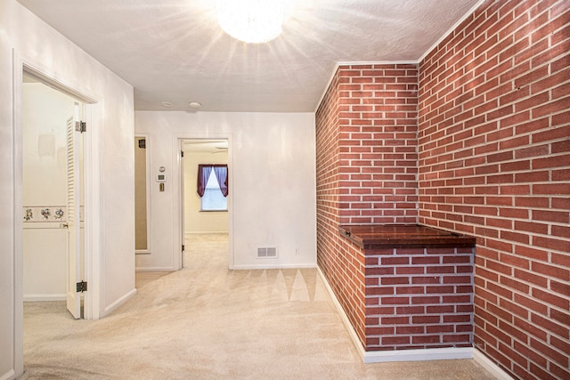 hall featuring light carpet, a textured ceiling, and brick wall