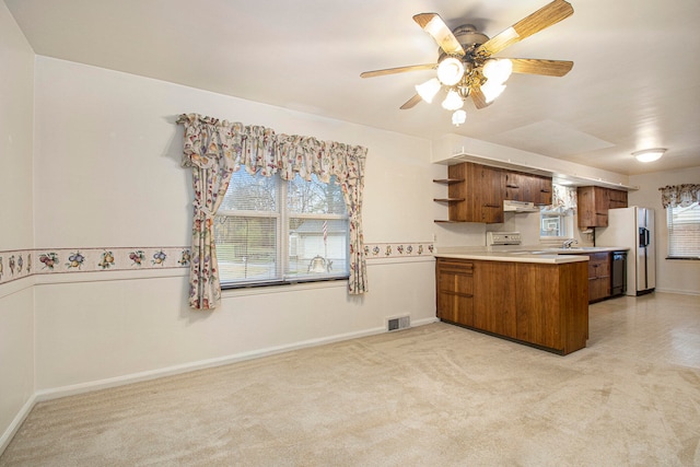 kitchen featuring kitchen peninsula, plenty of natural light, light colored carpet, and white appliances