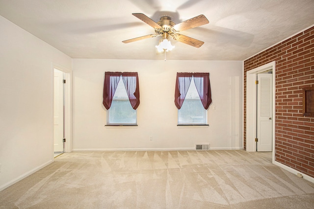 carpeted empty room with ceiling fan and brick wall