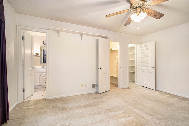 unfurnished bedroom featuring ceiling fan, light colored carpet, a spacious closet, and connected bathroom