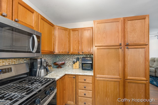 kitchen featuring tasteful backsplash, light stone countertops, stainless steel appliances, and hardwood / wood-style flooring