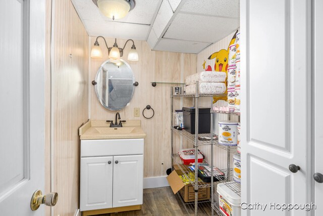 bathroom featuring a paneled ceiling, wood walls, vanity, and wood-type flooring