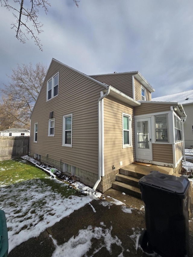 snow covered back of property featuring a sunroom