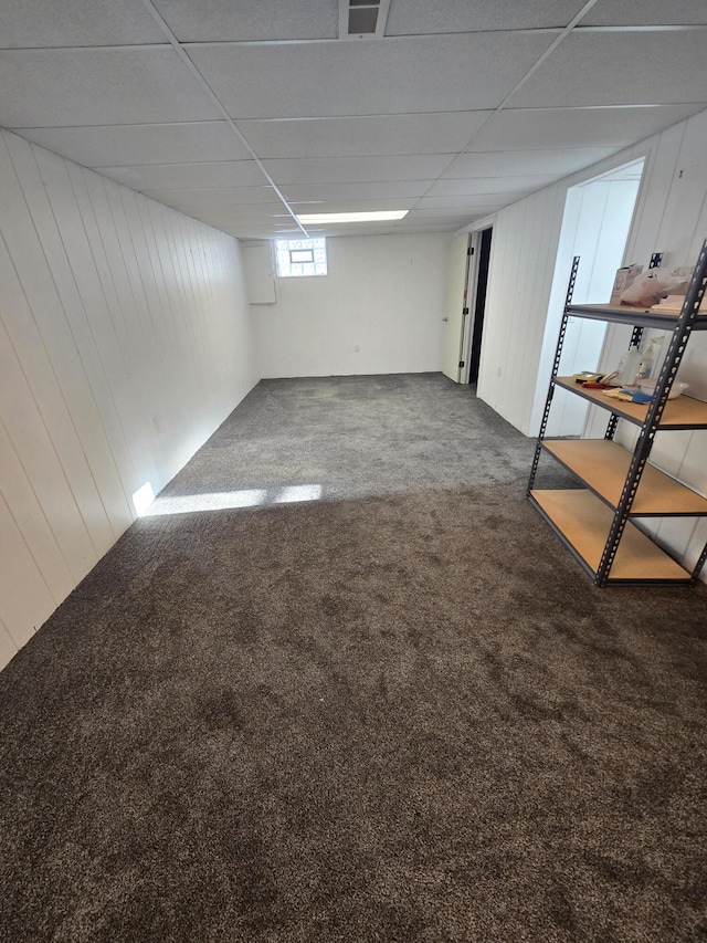 basement with carpet, a paneled ceiling, and wood walls