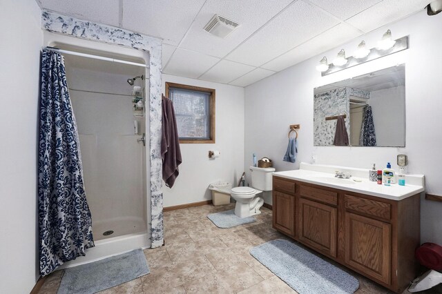 bathroom with a drop ceiling, vanity, tile patterned flooring, toilet, and walk in shower