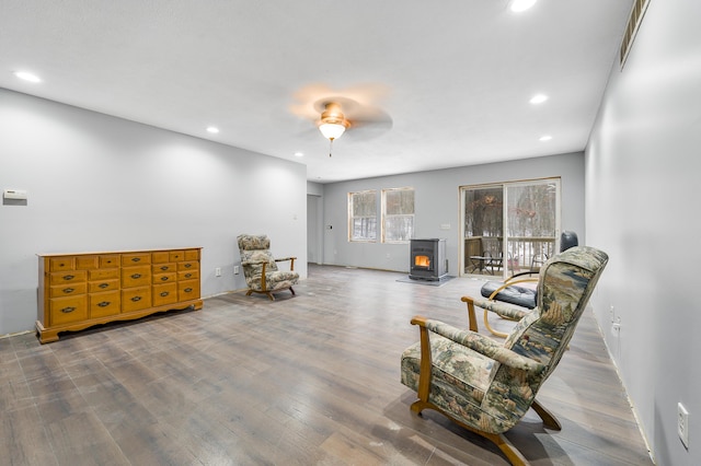 living area featuring hardwood / wood-style floors, ceiling fan, and a wood stove