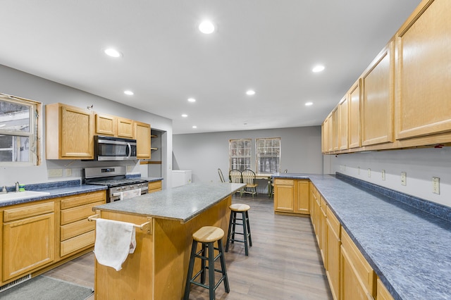 kitchen with appliances with stainless steel finishes, light wood-type flooring, light brown cabinetry, a center island, and a breakfast bar area