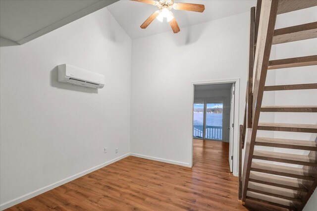 unfurnished room with stairway, ceiling fan, wood finished floors, a wall mounted air conditioner, and baseboards