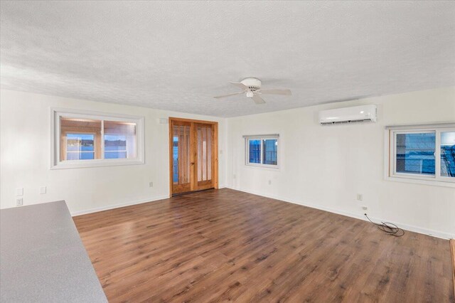 unfurnished room featuring baseboards, a ceiling fan, wood finished floors, a textured ceiling, and an AC wall unit