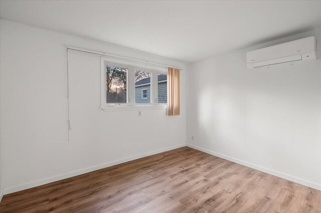 empty room featuring an AC wall unit, baseboards, and wood finished floors