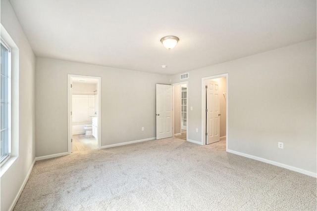 unfurnished bedroom with ensuite bathroom, a spacious closet, multiple windows, and light colored carpet