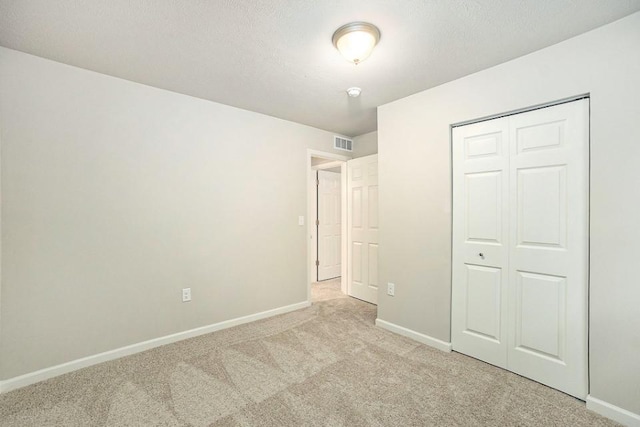 unfurnished bedroom featuring a closet, light colored carpet, and a textured ceiling