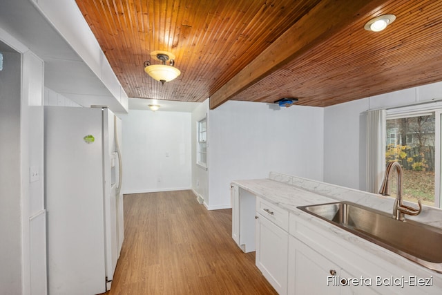 kitchen featuring light wood-type flooring, sink, white refrigerator with ice dispenser, beamed ceiling, and white cabinetry