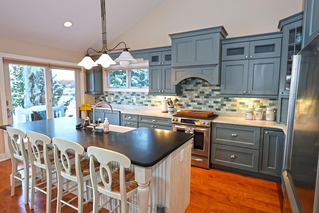 kitchen featuring backsplash, vaulted ceiling, an island with sink, appliances with stainless steel finishes, and dark hardwood / wood-style flooring