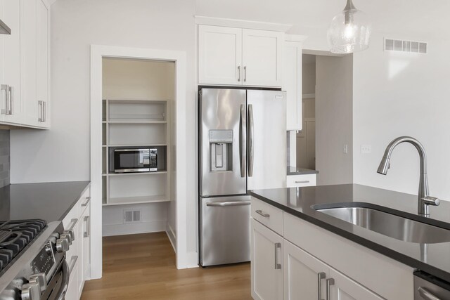 kitchen featuring stainless steel appliances, sink, wood-type flooring, white cabinetry, and hanging light fixtures