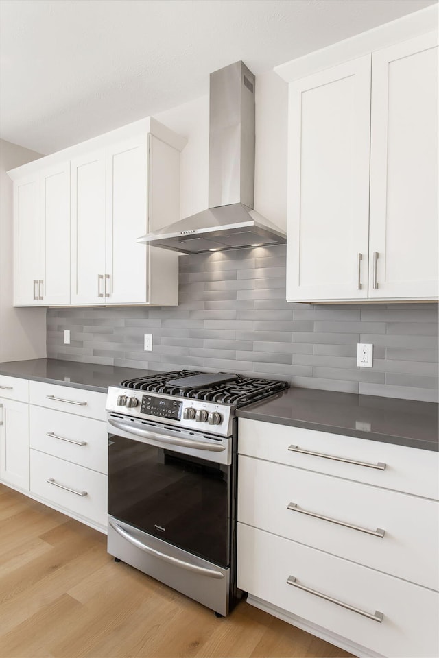 kitchen with white cabinetry, wall chimney range hood, stainless steel gas range, tasteful backsplash, and light wood-type flooring