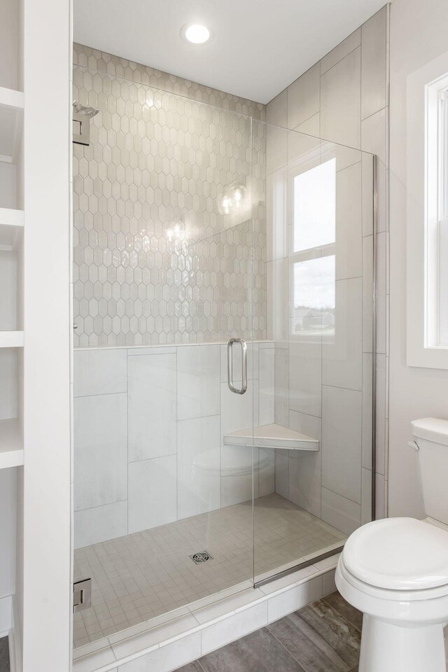 bathroom with hardwood / wood-style floors, a shower with door, and toilet