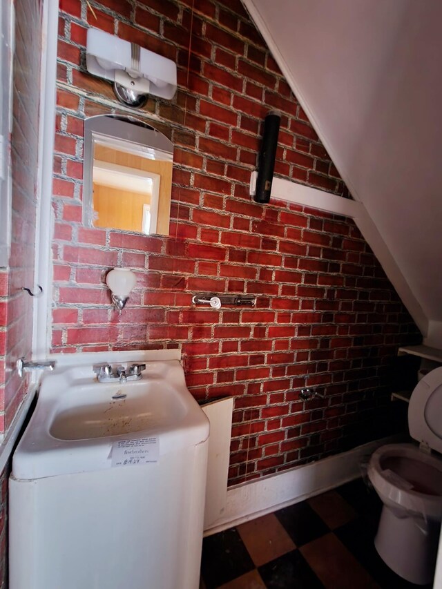 bathroom featuring brick wall and toilet