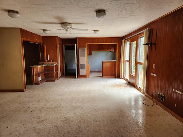 unfurnished living room featuring ceiling fan and wood walls