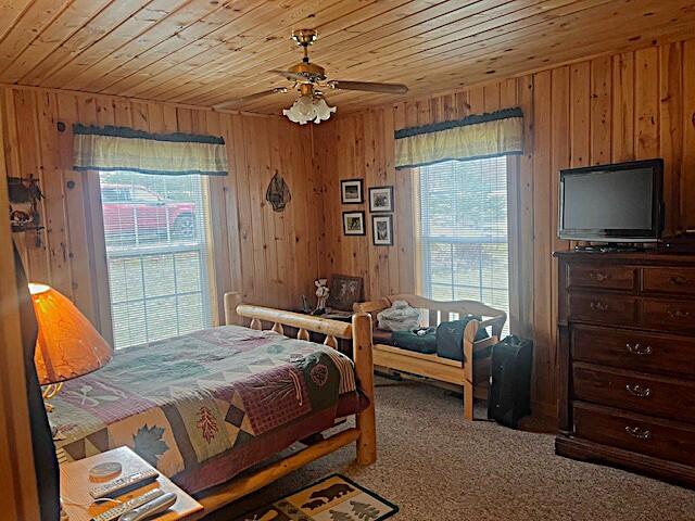 bedroom featuring carpet floors, ceiling fan, wooden walls, and wood ceiling