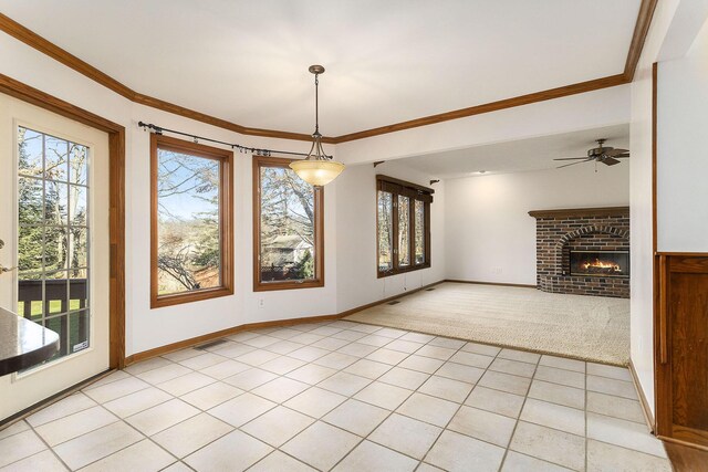 unfurnished dining area featuring ceiling fan, crown molding, light tile patterned floors, and a brick fireplace