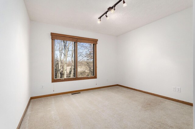 spare room with a textured ceiling, carpet floors, and track lighting