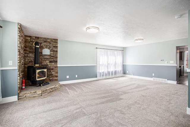 unfurnished living room with carpet, a textured ceiling, and a wood stove