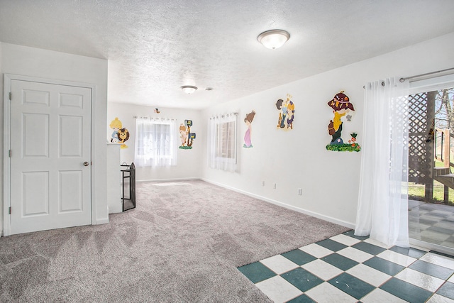 empty room with a textured ceiling, dark carpet, and plenty of natural light