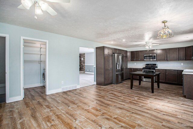 kitchen with appliances with stainless steel finishes, light wood-type flooring, backsplash, dark brown cabinets, and decorative light fixtures