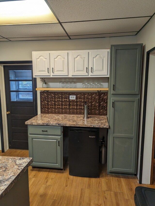 kitchen featuring white cabinets, a paneled ceiling, black refrigerator, and light wood-type flooring