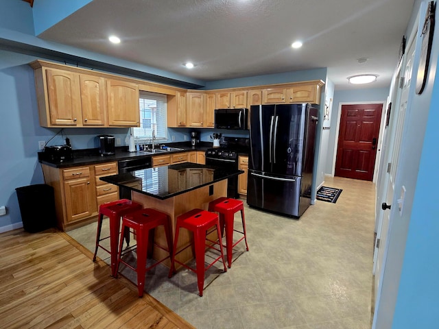 kitchen featuring a kitchen bar, light wood-type flooring, sink, black appliances, and a center island