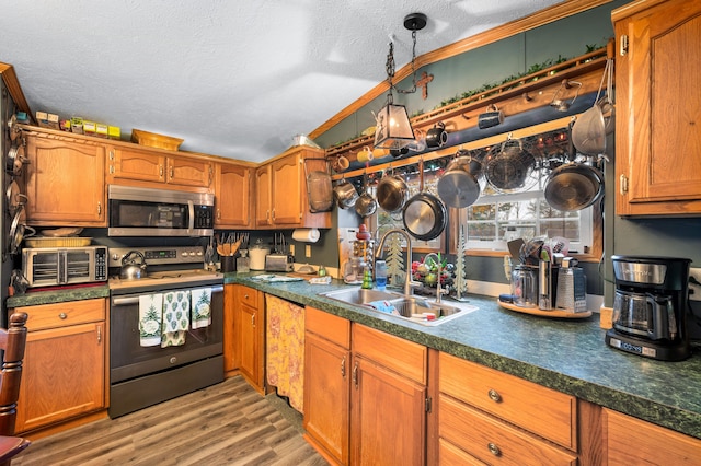 kitchen with a textured ceiling, stainless steel appliances, sink, light hardwood / wood-style flooring, and hanging light fixtures