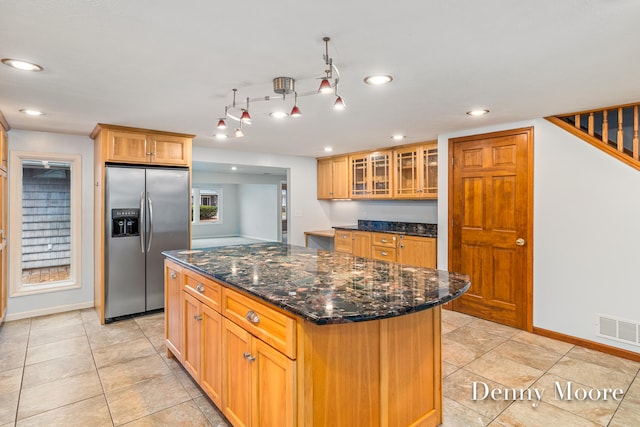 kitchen featuring stainless steel refrigerator with ice dispenser, light tile patterned floors, a kitchen island, and dark stone countertops