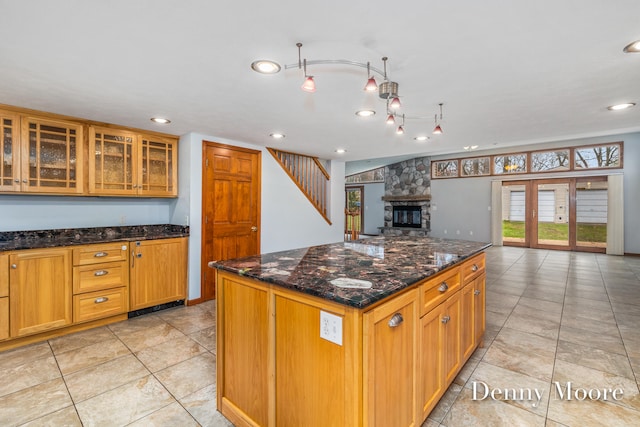 kitchen featuring a kitchen island, light tile patterned floors, a fireplace, and dark stone counters