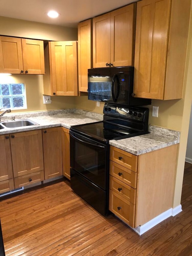 kitchen with light stone countertops, sink, black appliances, and light hardwood / wood-style floors