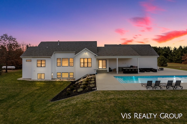 back house at dusk with outdoor lounge area, a patio, and a lawn