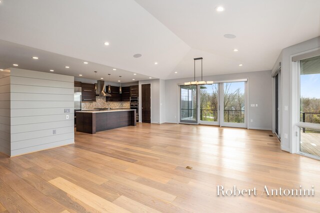 unfurnished living room featuring lofted ceiling, light wood-type flooring, a wealth of natural light, and an inviting chandelier