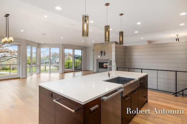 kitchen with light wood-type flooring, stainless steel dishwasher, a kitchen island with sink, and sink