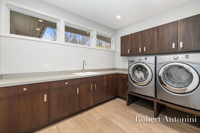 clothes washing area with washing machine and clothes dryer, sink, cabinets, and light hardwood / wood-style flooring