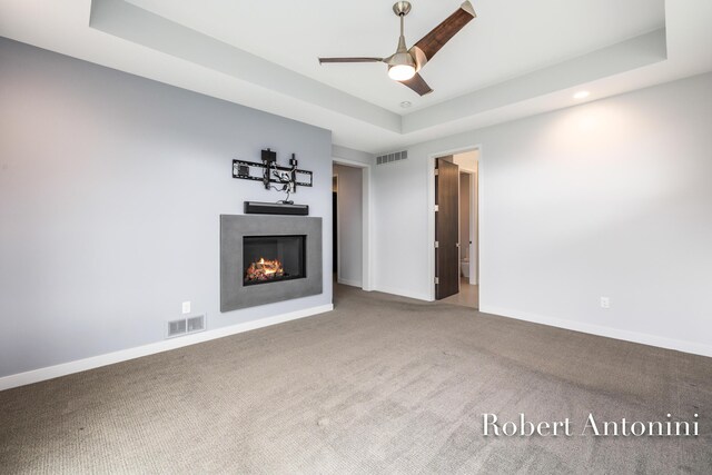 unfurnished living room featuring ceiling fan, carpet floors, and a tray ceiling