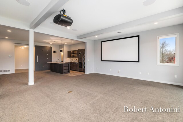 carpeted home theater room with beam ceiling