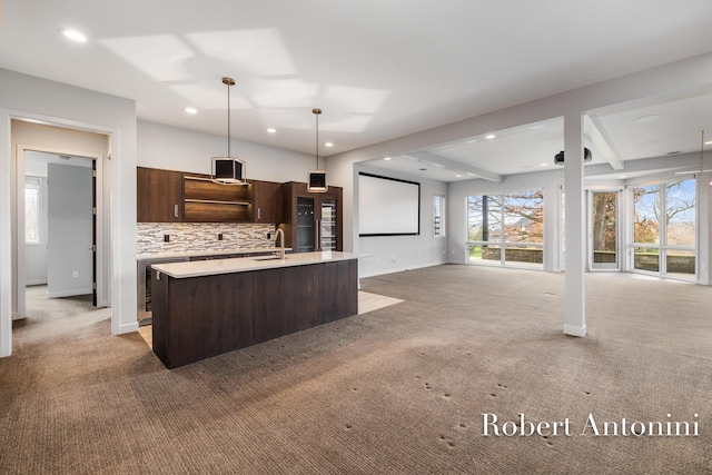 kitchen featuring decorative backsplash, a kitchen island with sink, light colored carpet, and hanging light fixtures