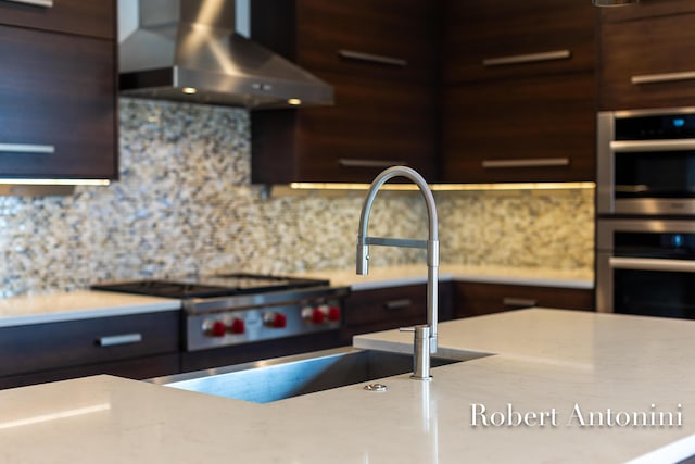 kitchen featuring wall chimney range hood, sink, wooden walls, tasteful backsplash, and stainless steel double oven