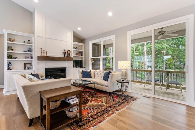 living room with built in features, vaulted ceiling, light hardwood / wood-style floors, and ceiling fan