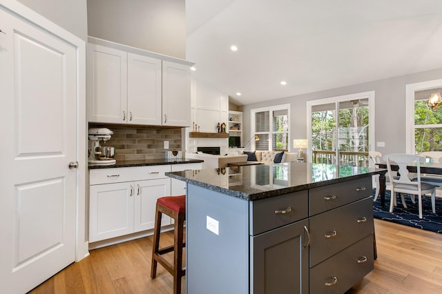 kitchen with dark stone counters, a center island, light wood-type flooring, and white cabinets