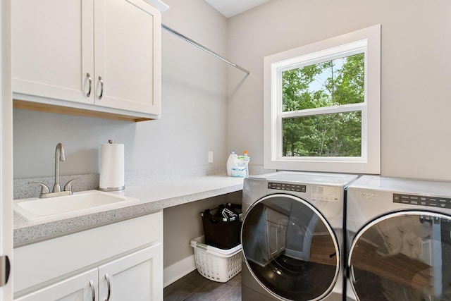 clothes washing area with sink, washing machine and dryer, cabinets, and dark tile patterned flooring