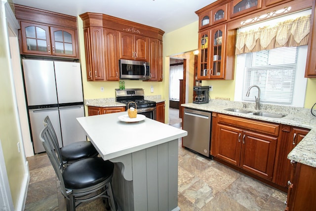 kitchen with light stone countertops, appliances with stainless steel finishes, a kitchen breakfast bar, sink, and a center island